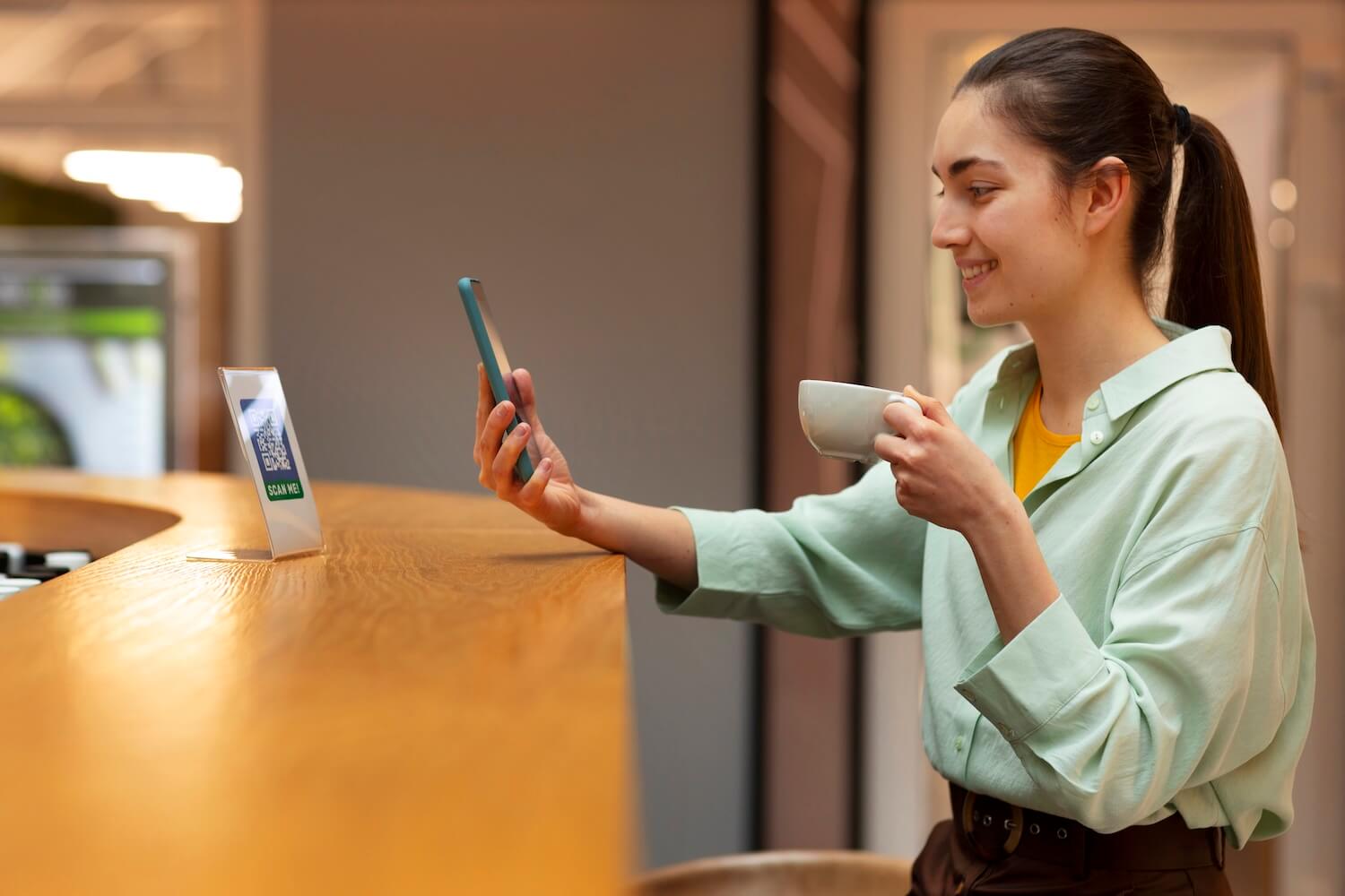 Női vállalkozó mobiltelefonnal és kávéval QR-kódot szkennel, digitális marketing eszközöket használva szépségipari üzletben
